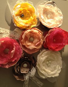 several different colored flowers are arranged on a table with white lace and ribbon around them