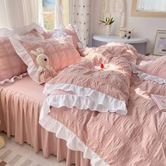 a bed with pink comforters and pillows in a small room next to a window