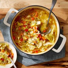 a pot filled with cabbage and carrots next to a bowl of soup on top of a wooden table