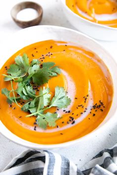 two white bowls filled with carrot soup and garnished with cilantro