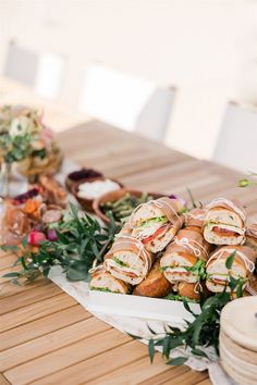 a table topped with lots of sandwiches on top of a wooden table covered in greenery