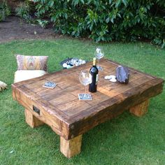 a wooden table sitting on top of a lush green grass covered field next to a bottle of wine