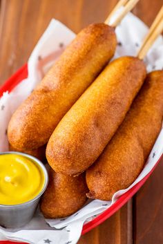 two hotdogs and mustard in a red basket on a wooden table with chopsticks