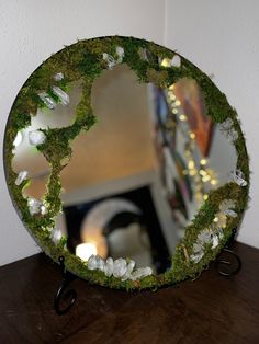 a mirror that is sitting on top of a table with moss and lights in the background