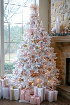 a white christmas tree decorated with pink and gold ornaments in front of a fire place