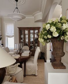 a vase with white flowers on top of a table next to a lamp and chair