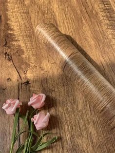 three pink roses sitting on top of a wooden table next to a roll of string