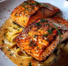 two pieces of salmon on top of pasta in a white bowl with garnish