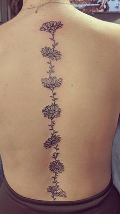 the back of a woman's neck with flowers on it and an arrow tattoo