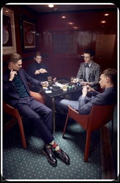 three men sitting at a table playing cards in a room with dark walls and carpet