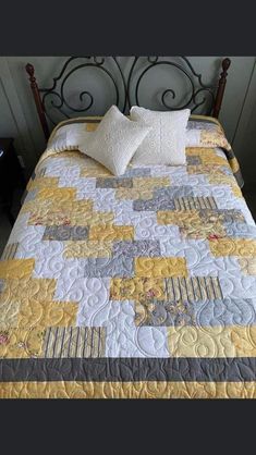 a bed with yellow and gray quilts on it's headboard, next to a night stand