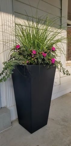 a tall black planter with pink flowers in it