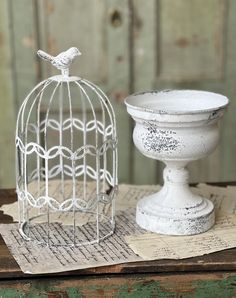 a white birdcage sitting on top of a piece of paper next to a vase