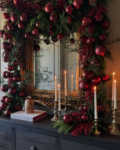 a christmas mantle with candles and ornaments on it in front of a mirror, decorated with greenery