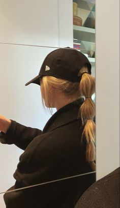 a woman sitting in front of a mirror wearing a baseball cap and holding a cell phone