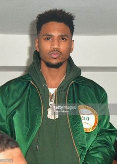 a young man wearing a green jacket and standing in front of a wall