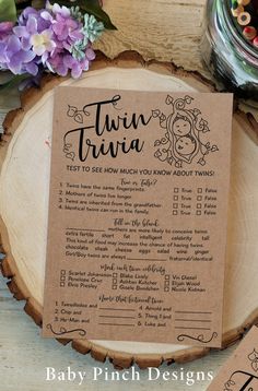 a baby shower checklist on a wood slice with purple flowers and twin trivia stickers