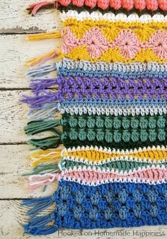 a multicolored crocheted blanket with fringes on it sitting on top of a wooden table