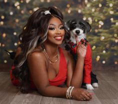 a beautiful woman holding a small dog in her lap while sitting on the floor next to a christmas tree