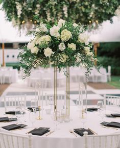 a table with white flowers and greenery in tall vases on top of it