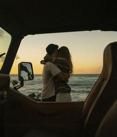 a man and woman embracing in the back of a truck near the ocean at sunset