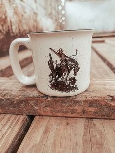 a white coffee cup with an image of a cowboy on it sitting on a wooden table