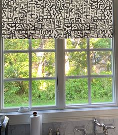 a kitchen window covered in black and white roman shades