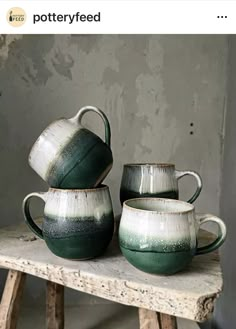 three green and white ceramic cups sitting on top of a wooden table next to a wall