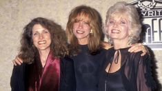 three women standing next to each other in front of a wall