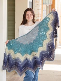 a woman is holding up a crocheted blanket