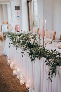 a long table with candles and greenery on the top is set up for a wedding reception