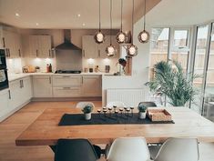 a dining room table with chairs and lights hanging from it's ceiling in a kitchen