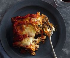 a piece of lasagna on a plate with a fork and glass of wine