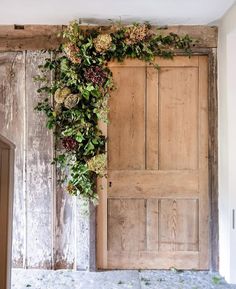 an old wooden door covered in flowers and greenery next to a wood paneled wall