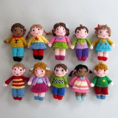 a group of knitted dolls sitting next to each other on a white surface in front of a wall