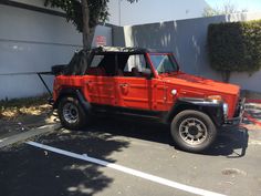 an orange jeep parked in a parking lot next to a wall and tree with no leaves on it