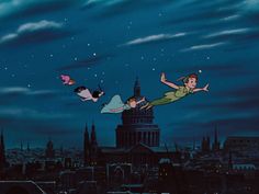 two people flying in the air over a city at night with buildings and clouds behind them