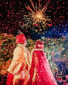 two people dressed in red and white standing next to each other with fireworks behind them