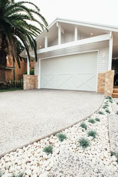 a white house with a palm tree in the front yard and landscaping on the side