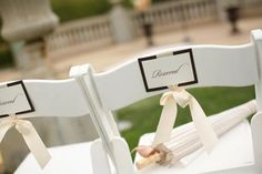 two white chairs with ribbons tied to them and name tags on the back of each chair