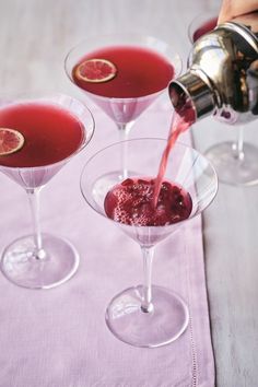 two martini glasses filled with red liquid being poured into them