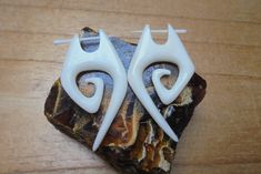 two white earrings sitting on top of a piece of rock next to a pair of scissors