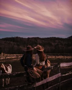 two people are sitting on a fence with horses