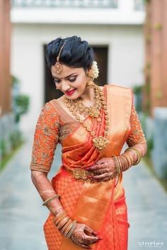 a woman in an orange and gold sari is posing for the camera with her hands on her hips