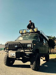 a man sitting on top of a green truck with lights on it's roof