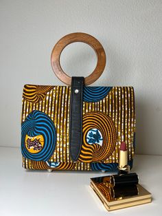 This gorgeous Aisha African Print Hand Bag is perfect for travel, work, or parties. Our light bag is sourced from Ghana and made of Authentic African print fabric with stitch details for a luxe look and are wooden handle. The Interior accessory and pockets help you keep items organized in your purse. This bag is individually handcrafted and lovingly made to be unique to you Description: African Print handbag with Wooden handle The inner is fully lined with black fabric Interior compartments for Rectangular Clutch With Leather Handles For Travel, Rectangular Clutch With Leather Handles For Daily Use, Multicolor Rectangular Shoulder Bag With Bamboo Handle, Daily Use Clutch With Detachable Round Handle, Leather Handle Clutch Satchel For On-the-go, Clutch With Detachable Round Handle For Daily Use, Multicolor Bag With Round Handle For Daily Use, Multicolor Bags With Round Handle For Daily Use, Daily Use Multicolor Bags With Round Handle