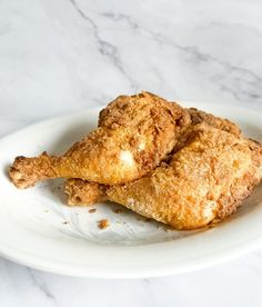 two fried chicken on a white plate sitting on a marble counter top next to a fork and knife