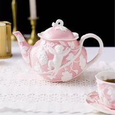 a pink tea pot sitting on top of a table next to a cup and saucer