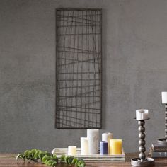 a wooden table topped with candles next to a metal wall hanging on a gray wall