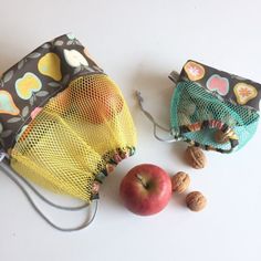 two small drawsacks are next to an apple and nuts on a white surface